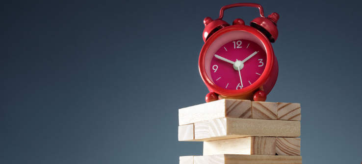A red alarm clock sits atop a jenga tower